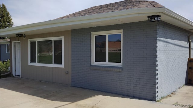 view of side of property with roof with shingles, a patio, and brick siding