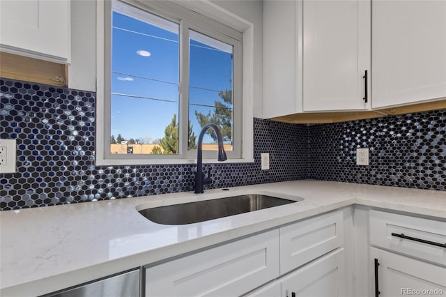 kitchen with decorative backsplash, light stone countertops, dishwasher, a sink, and white cabinetry