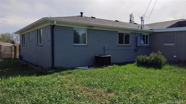 back of house with fence, a shingled roof, brick siding, central AC unit, and a yard