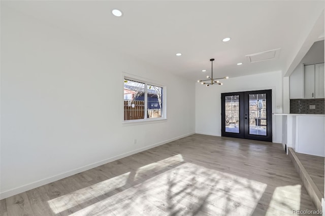 empty room with french doors, a chandelier, and light hardwood / wood-style flooring