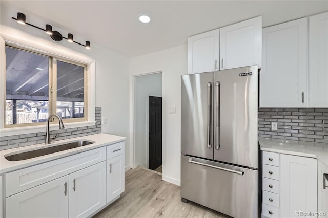 kitchen featuring high end refrigerator, backsplash, sink, light hardwood / wood-style flooring, and white cabinets