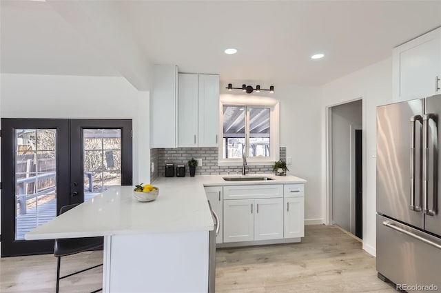 kitchen with high quality fridge, a sink, a kitchen breakfast bar, white cabinets, and tasteful backsplash