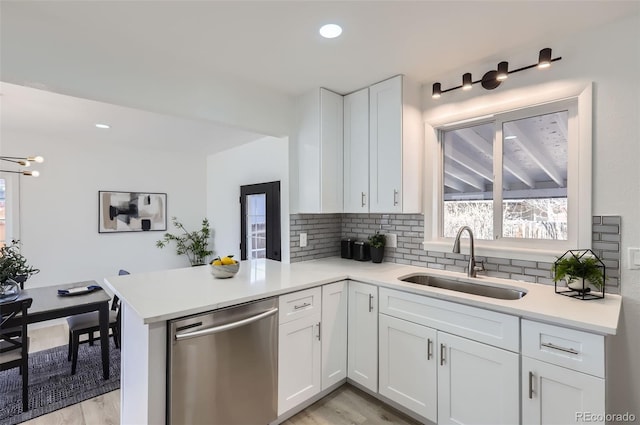 kitchen featuring light countertops, stainless steel dishwasher, white cabinets, a sink, and a peninsula