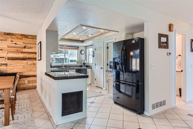 kitchen with visible vents, a peninsula, dark countertops, light tile patterned floors, and black fridge