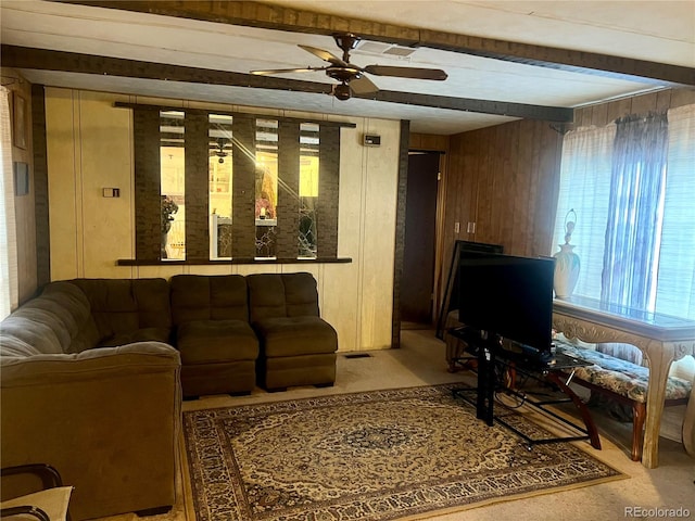 carpeted living room with wood walls, beamed ceiling, and ceiling fan