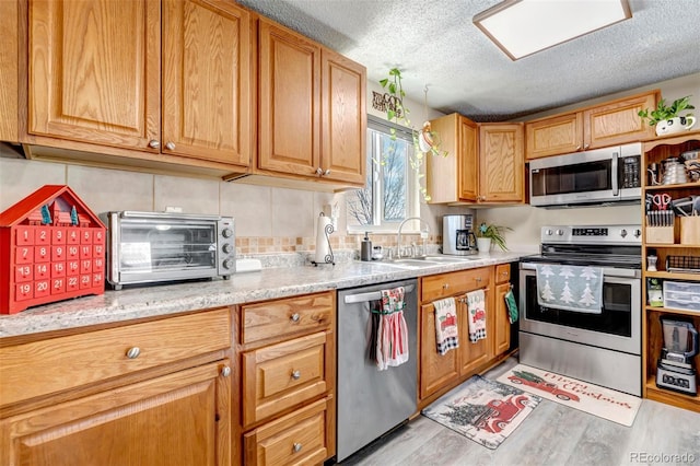 kitchen with sink, light hardwood / wood-style floors, a textured ceiling, decorative backsplash, and appliances with stainless steel finishes