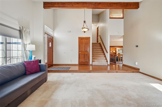 living room featuring baseboards, stairway, beam ceiling, carpet flooring, and a towering ceiling