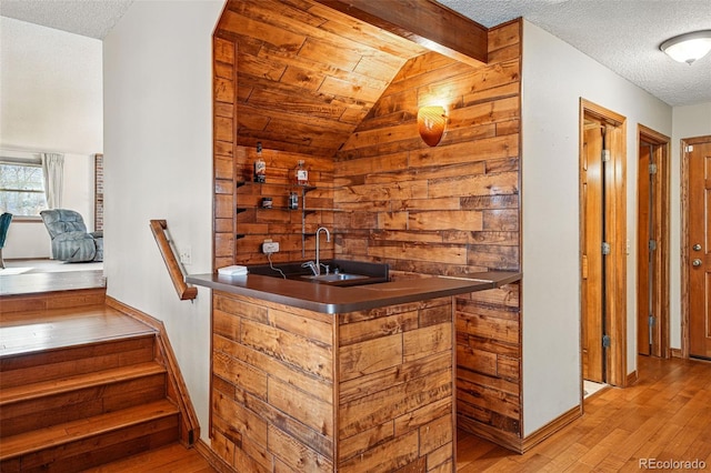 bar featuring vaulted ceiling with beams, baseboards, hardwood / wood-style floors, wet bar, and a textured ceiling