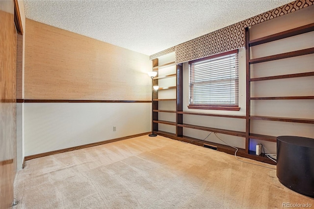 carpeted empty room with wallpapered walls, baseboards, and a textured ceiling