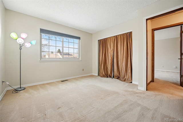 unfurnished bedroom featuring visible vents, a textured ceiling, baseboards, and carpet floors