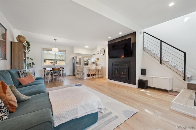 living area featuring recessed lighting, wood finished floors, stairway, and a fireplace