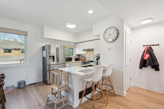 kitchen with a breakfast bar area, visible vents, appliances with stainless steel finishes, a peninsula, and under cabinet range hood