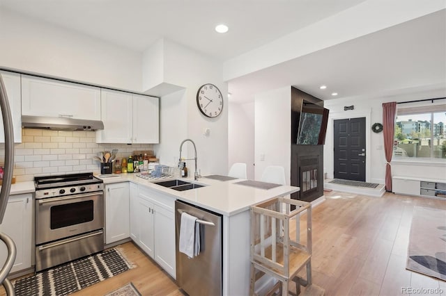 kitchen with appliances with stainless steel finishes, a sink, a peninsula, light wood-type flooring, and under cabinet range hood