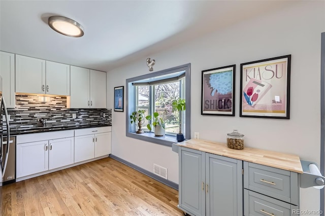 kitchen featuring backsplash, visible vents, a sink, white cabinets, and light wood finished floors