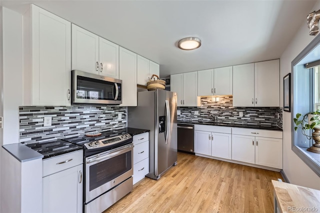 kitchen featuring dark countertops, light wood-style floors, tasteful backsplash, a sink, and appliances with stainless steel finishes