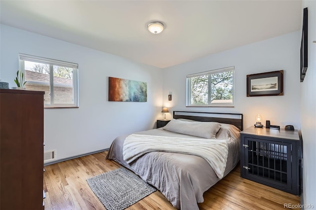 bedroom featuring baseboards, visible vents, multiple windows, and wood finished floors