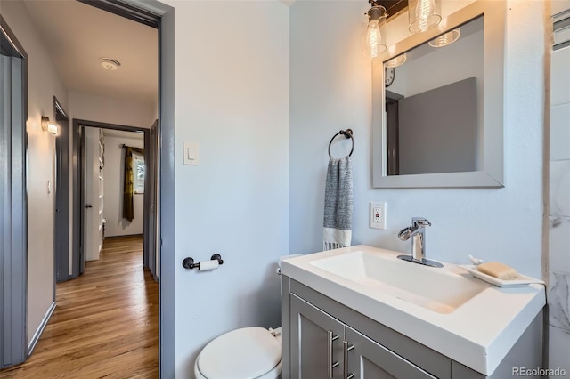 half bath with vanity, baseboards, toilet, and wood finished floors