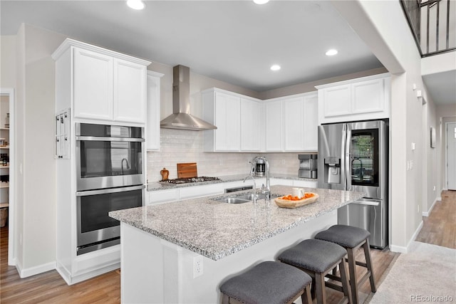 kitchen featuring appliances with stainless steel finishes, wall chimney exhaust hood, sink, light hardwood / wood-style floors, and white cabinetry