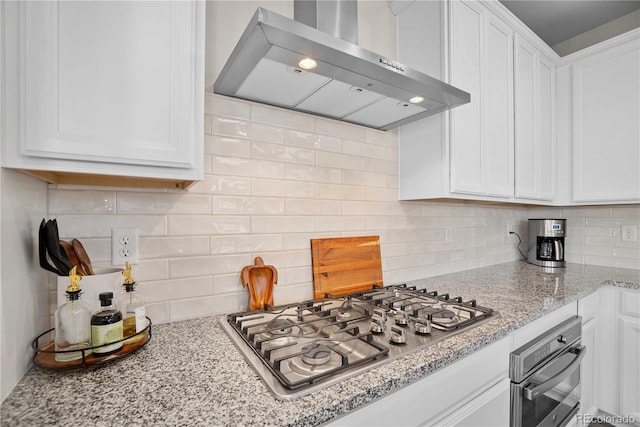 kitchen with tasteful backsplash, white cabinetry, wall chimney range hood, and appliances with stainless steel finishes