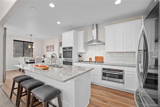 kitchen featuring wall chimney exhaust hood, stainless steel appliances, sink, pendant lighting, and white cabinetry