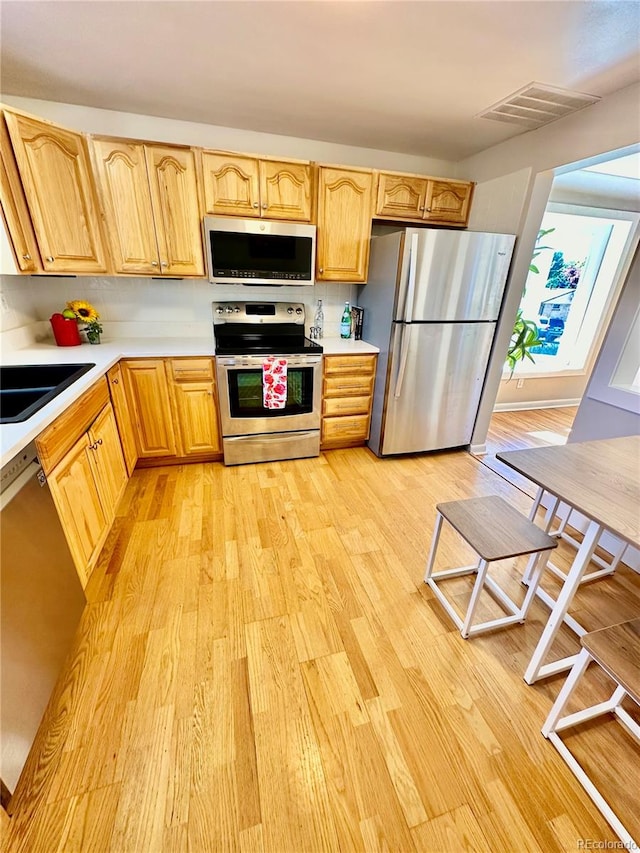 kitchen with appliances with stainless steel finishes, sink, light wood-type flooring, and backsplash