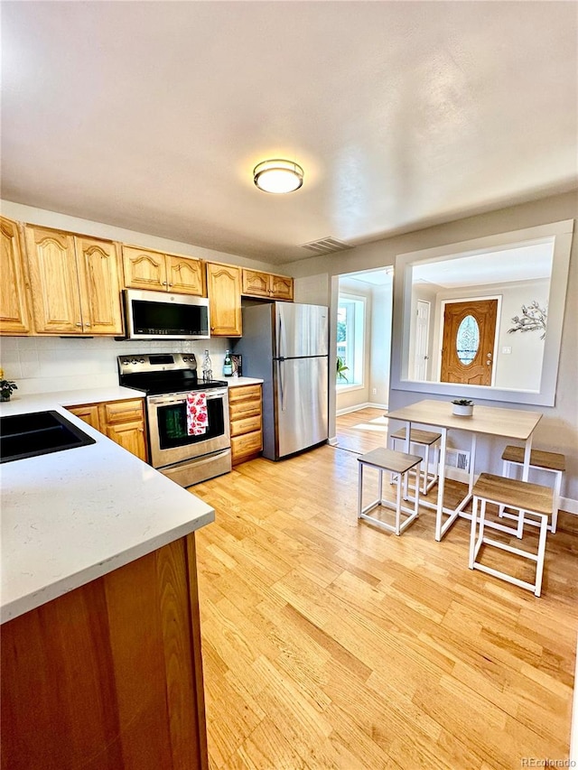 kitchen with light hardwood / wood-style flooring, appliances with stainless steel finishes, sink, and decorative backsplash