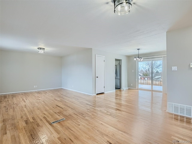 unfurnished room featuring an inviting chandelier and light hardwood / wood-style flooring