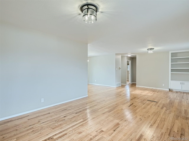 unfurnished living room featuring built in shelves and light hardwood / wood-style floors