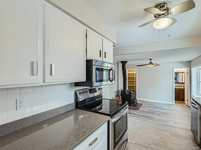 kitchen with light stone countertops, a wood stove, white cabinets, and appliances with stainless steel finishes