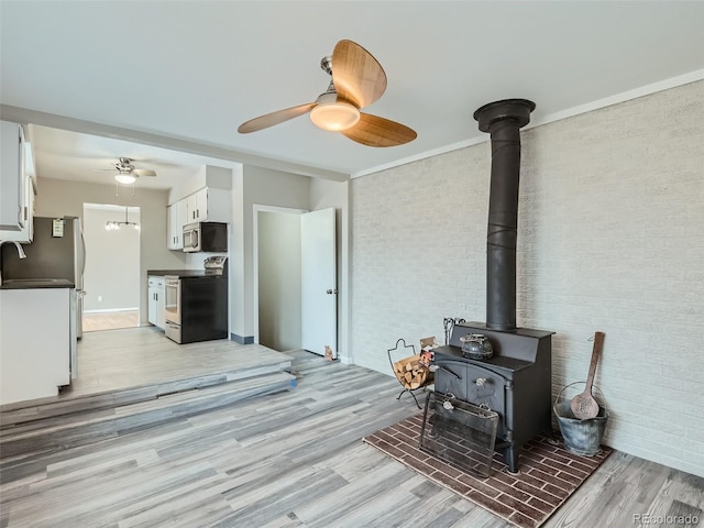 living room with sink, light hardwood / wood-style flooring, ceiling fan, brick wall, and a wood stove