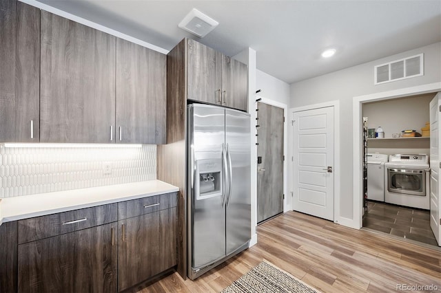 kitchen featuring decorative backsplash, washer and clothes dryer, stainless steel refrigerator with ice dispenser, dark brown cabinets, and light wood-type flooring