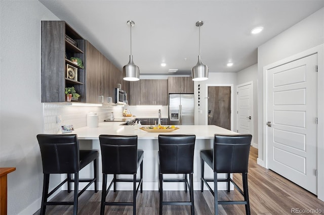 kitchen with decorative light fixtures, backsplash, a kitchen breakfast bar, kitchen peninsula, and stainless steel appliances