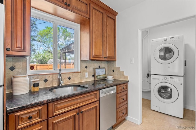1177 Wabash St, Denver, CO 80220 - kitchen featuring dishwasher, stacked washer / drying machine, brown cabinetry, and dark stone counters