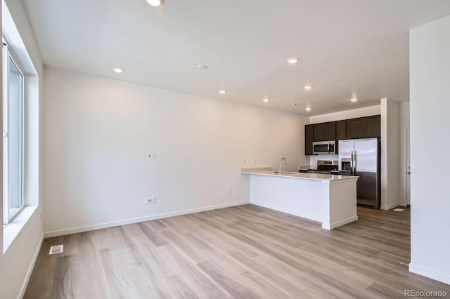 kitchen with light wood-type flooring, a peninsula, visible vents, and appliances with stainless steel finishes