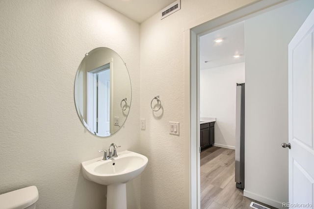 bathroom with wood finished floors, visible vents, toilet, and a textured wall