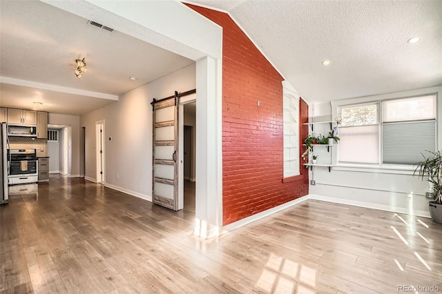 interior space with hardwood / wood-style flooring, a barn door, a textured ceiling, and brick wall