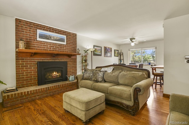 living room with hardwood / wood-style floors, a brick fireplace, and ceiling fan