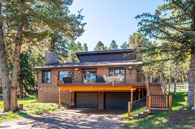 25357 Snyder Ave, Conifer, CO 80433 - view of front facade with brick siding, a garage, stairs, a chimney, and driveway