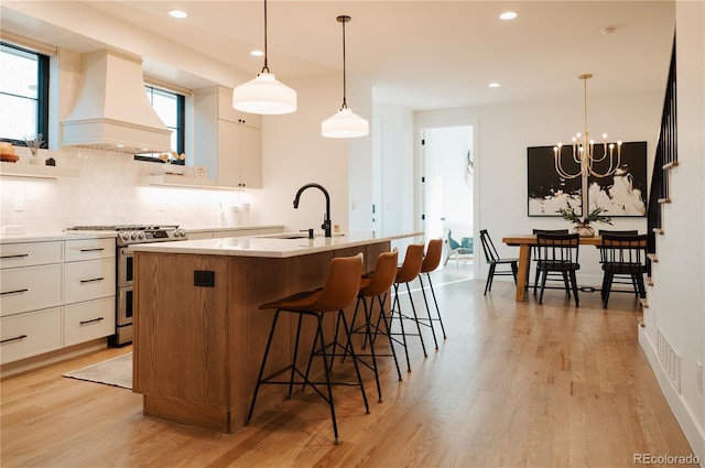 kitchen featuring a sink, tasteful backsplash, white cabinetry, range with two ovens, and custom exhaust hood