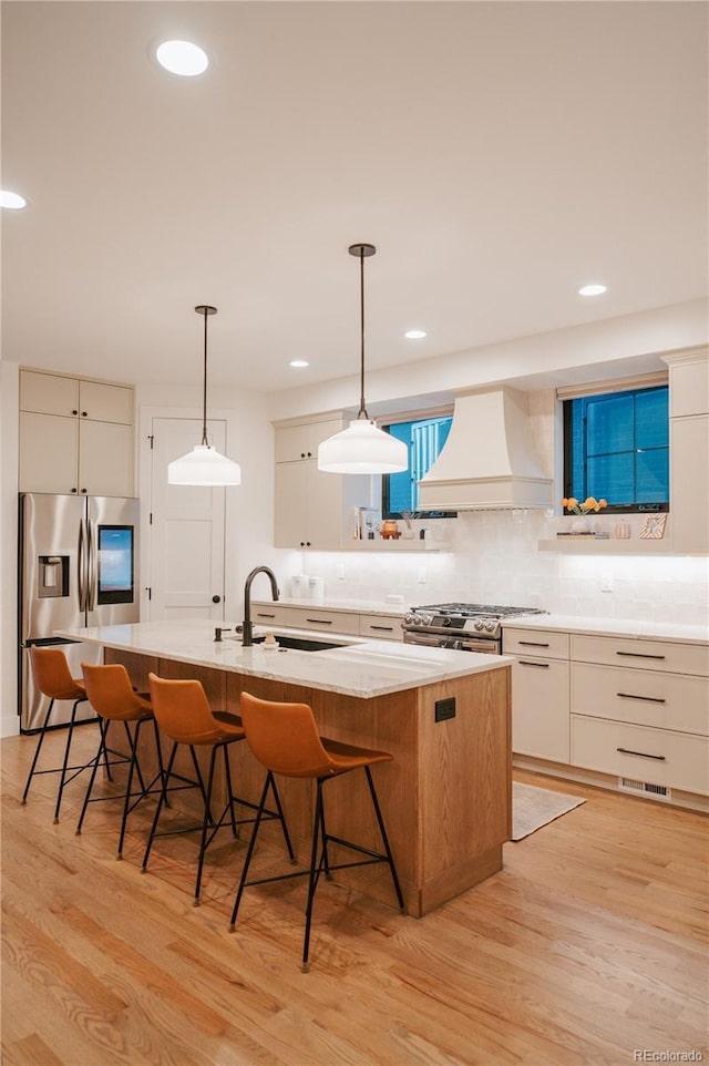 kitchen featuring custom exhaust hood, a sink, stainless steel appliances, light wood-style floors, and a kitchen breakfast bar