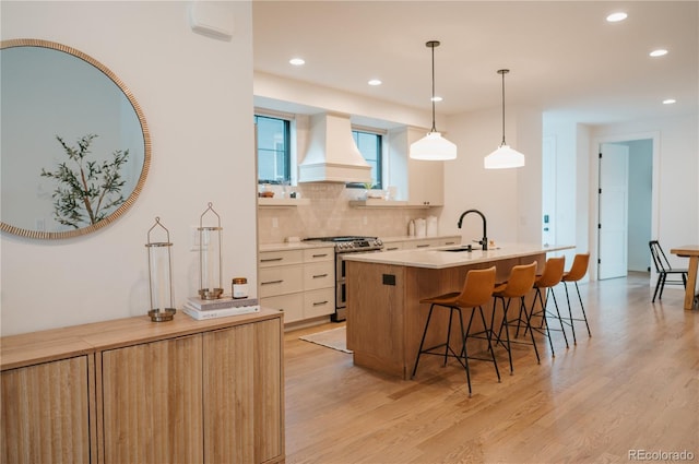 kitchen with a breakfast bar area, custom exhaust hood, range with two ovens, a sink, and light wood-style floors