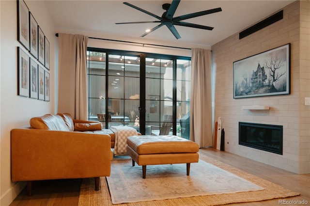 sitting room featuring a large fireplace, ceiling fan, and wood finished floors