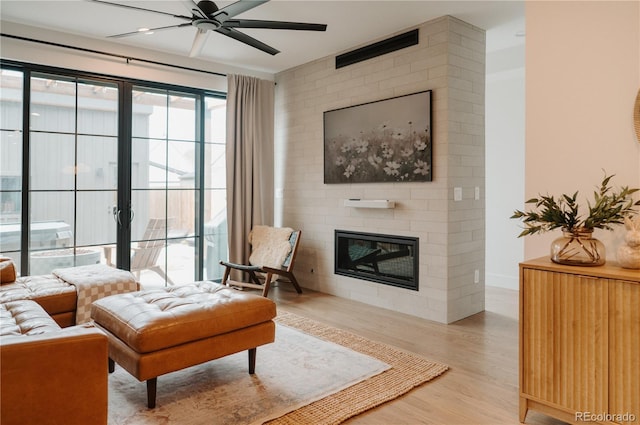 living area featuring ceiling fan, baseboards, light wood-type flooring, and a large fireplace