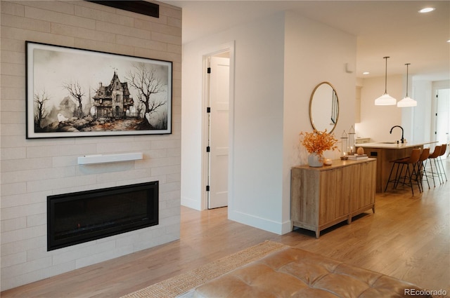 living room featuring recessed lighting, light wood-type flooring, baseboards, and a glass covered fireplace