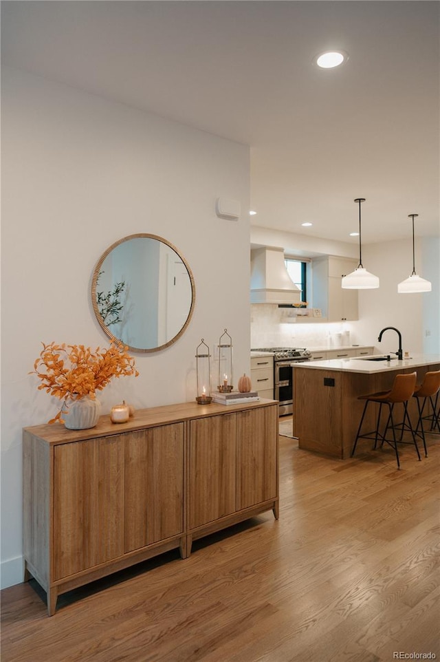 kitchen featuring premium range hood, a breakfast bar, range with two ovens, light wood-style floors, and tasteful backsplash