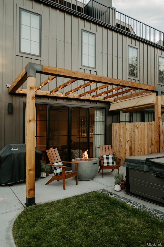 rear view of house with fence, an outdoor fire pit, a hot tub, a patio area, and board and batten siding