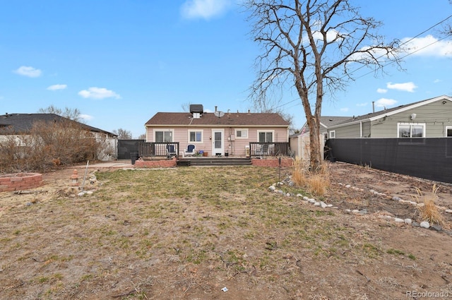 rear view of property featuring fence, a lawn, and a wooden deck