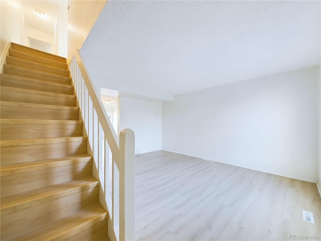 staircase with a textured ceiling and hardwood / wood-style flooring