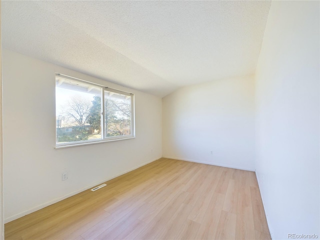 unfurnished room featuring light hardwood / wood-style floors, a textured ceiling, and lofted ceiling