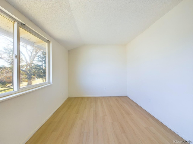 spare room featuring lofted ceiling, light wood-type flooring, and a textured ceiling